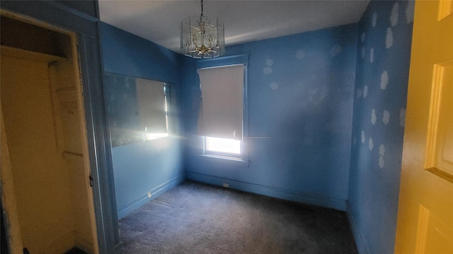 carpeted empty room featuring a chandelier and baseboards