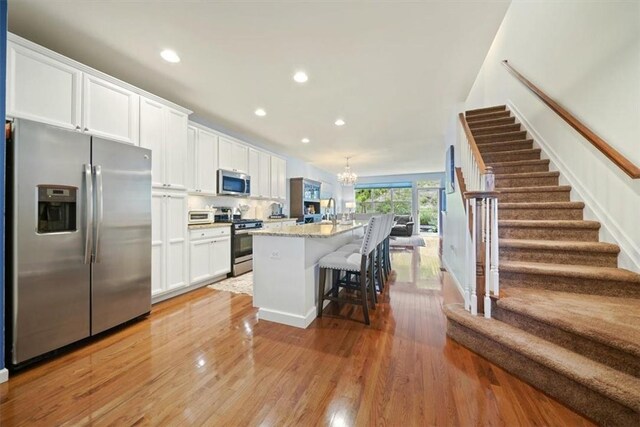 kitchen featuring white cabinets, appliances with stainless steel finishes, light stone countertops, and an island with sink