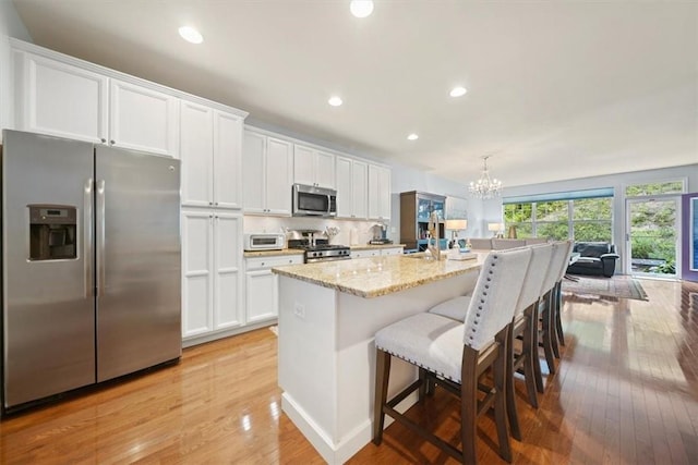 kitchen with a center island with sink, decorative light fixtures, white cabinets, and stainless steel appliances