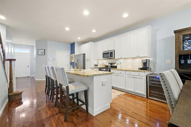 kitchen featuring sink, an island with sink, wood-type flooring, white cabinets, and appliances with stainless steel finishes