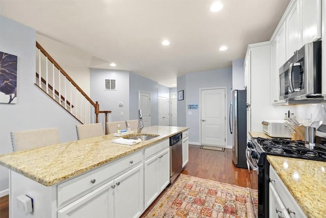 kitchen with a center island with sink, light hardwood / wood-style flooring, light stone counters, white cabinetry, and stainless steel appliances