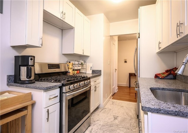 kitchen with dark stone counters, sink, light hardwood / wood-style flooring, white cabinets, and stainless steel range with gas cooktop