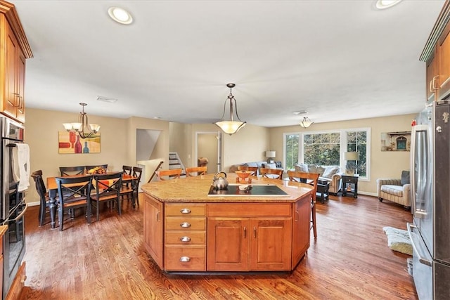 kitchen with stainless steel fridge, dark wood-type flooring, pendant lighting, a chandelier, and an island with sink