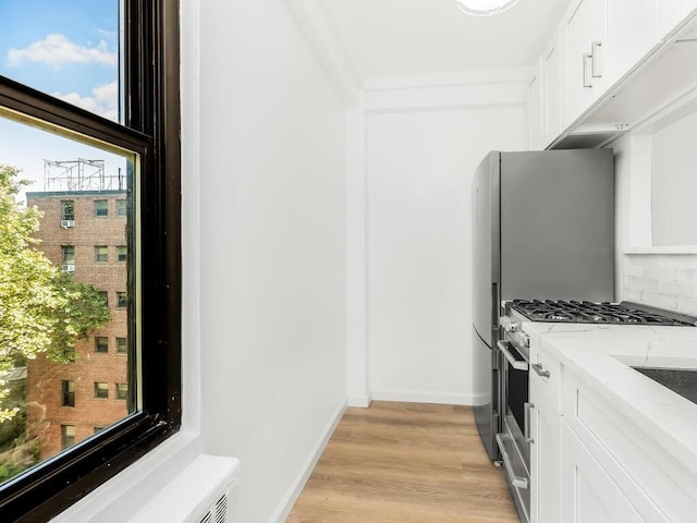 kitchen with decorative backsplash, light stone countertops, light hardwood / wood-style flooring, high end stainless steel range, and white cabinets