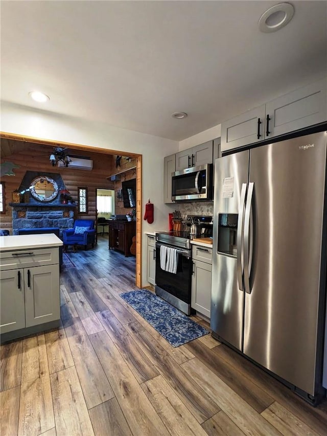 kitchen with tasteful backsplash, gray cabinetry, stainless steel appliances, wooden walls, and hardwood / wood-style floors