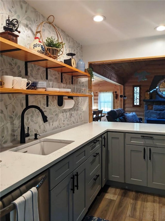 kitchen with light stone countertops, dark hardwood / wood-style flooring, stainless steel dishwasher, and sink