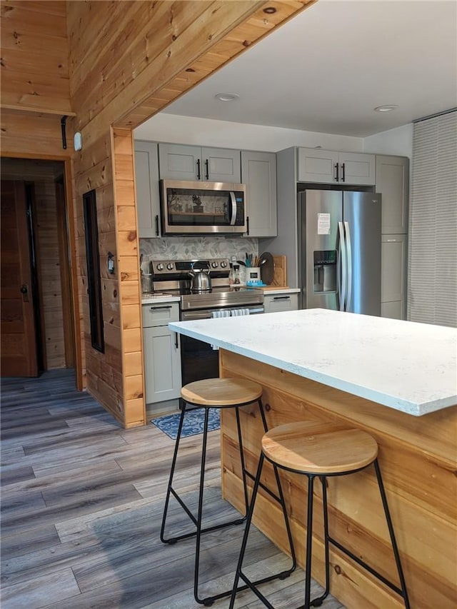 kitchen with gray cabinets, wooden walls, a breakfast bar, and stainless steel appliances