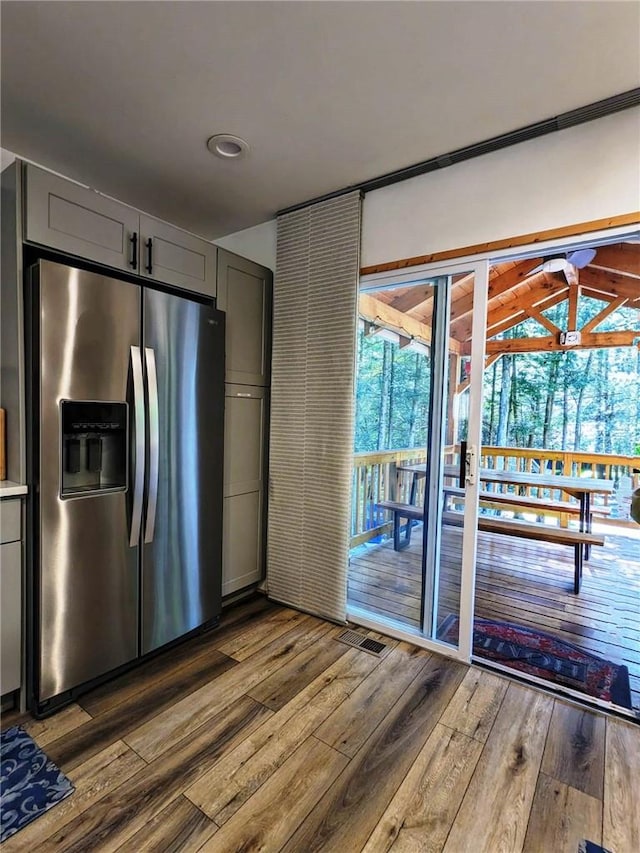 kitchen with gray cabinets, stainless steel fridge, hardwood / wood-style flooring, and vaulted ceiling