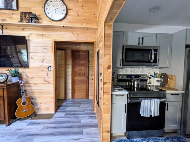 kitchen with gray cabinetry, wooden walls, light hardwood / wood-style flooring, and stainless steel appliances