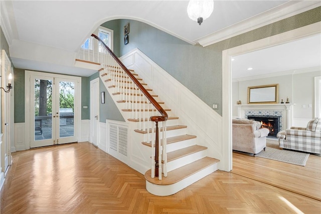 staircase with a tile fireplace, french doors, parquet floors, and crown molding