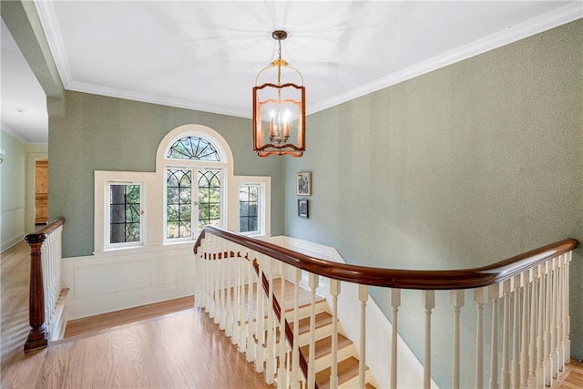 stairs with wood-type flooring, ornamental molding, and an inviting chandelier