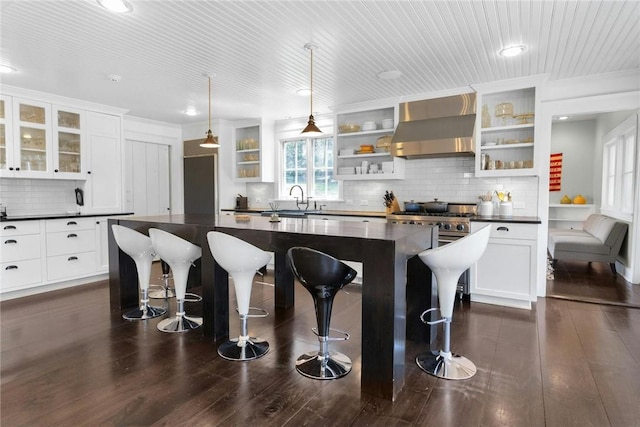 kitchen with a kitchen bar, dark wood-type flooring, sink, wall chimney range hood, and a kitchen island