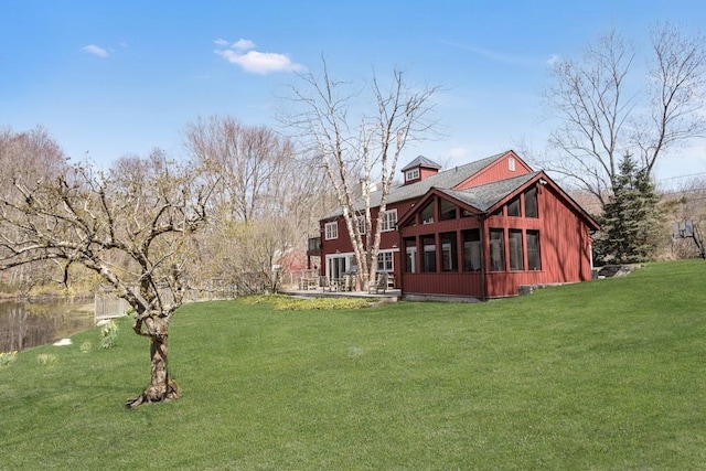 rear view of property with a sunroom, a yard, and a water view