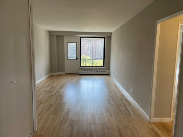 unfurnished room with a baseboard heating unit and light hardwood / wood-style flooring