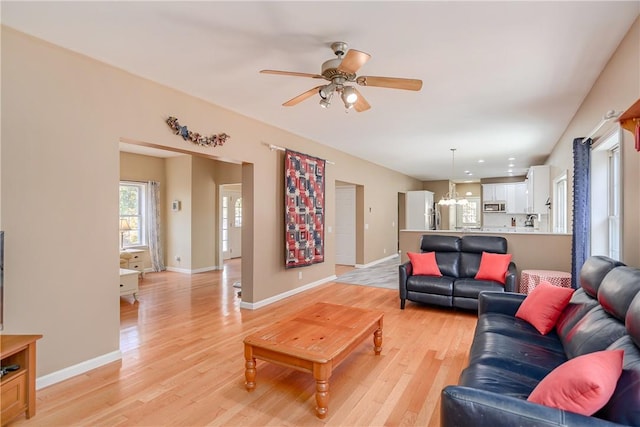 living room with ceiling fan with notable chandelier and light hardwood / wood-style floors