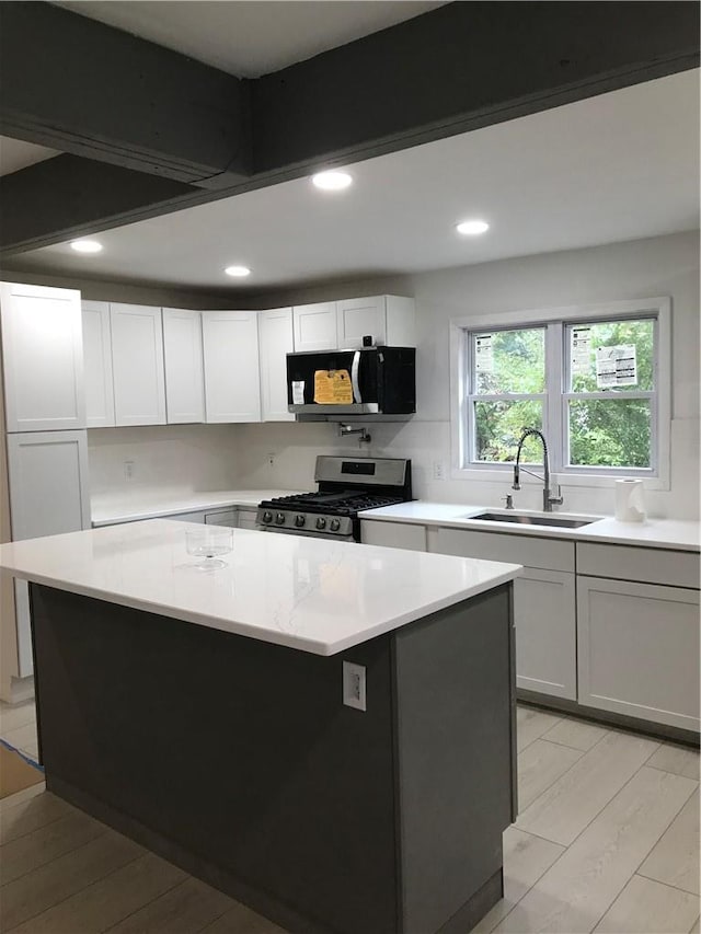 kitchen featuring a center island, stainless steel gas stove, sink, light hardwood / wood-style floors, and white cabinets