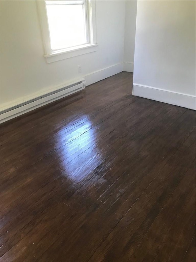 empty room with dark hardwood / wood-style flooring and baseboard heating