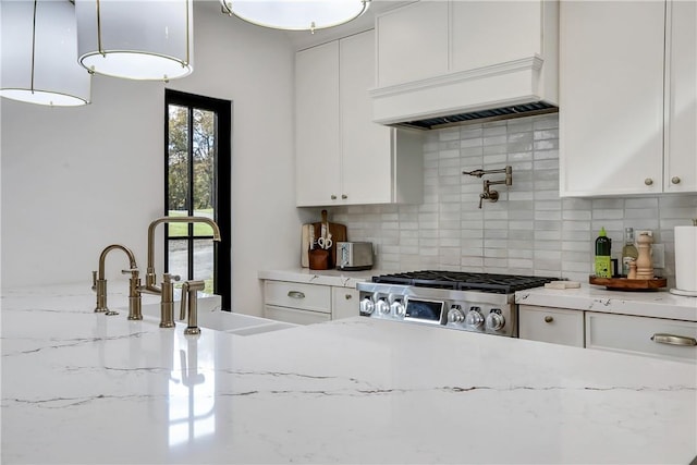 kitchen with decorative backsplash, white cabinetry, stainless steel range, and light stone counters