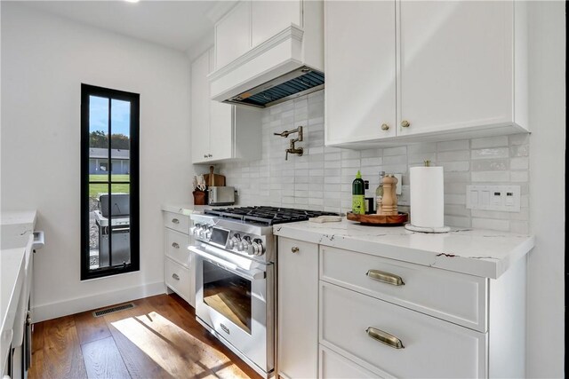 kitchen with dark wood-type flooring, high end stove, decorative backsplash, white cabinets, and custom exhaust hood