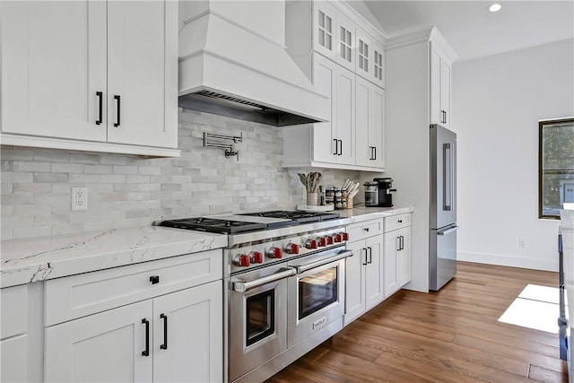 kitchen with high end appliances, white cabinets, hardwood / wood-style flooring, decorative backsplash, and custom range hood