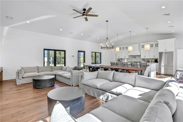 living room with lofted ceiling, ceiling fan with notable chandelier, and hardwood / wood-style flooring