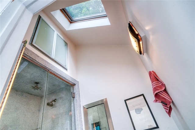 bathroom featuring a skylight, ceiling fan, high vaulted ceiling, and walk in shower