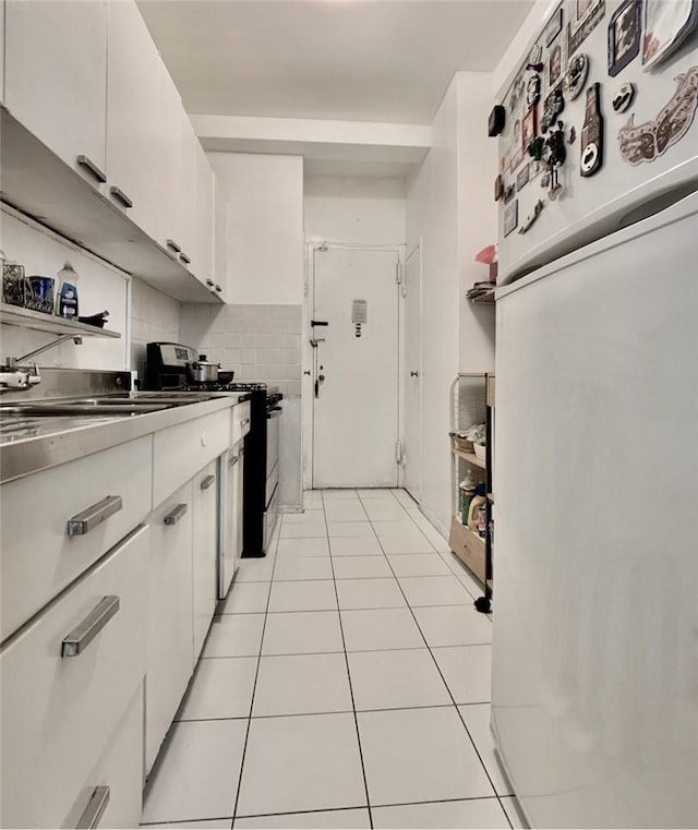 kitchen with light tile patterned flooring, white cabinets, white fridge, and black range with gas cooktop