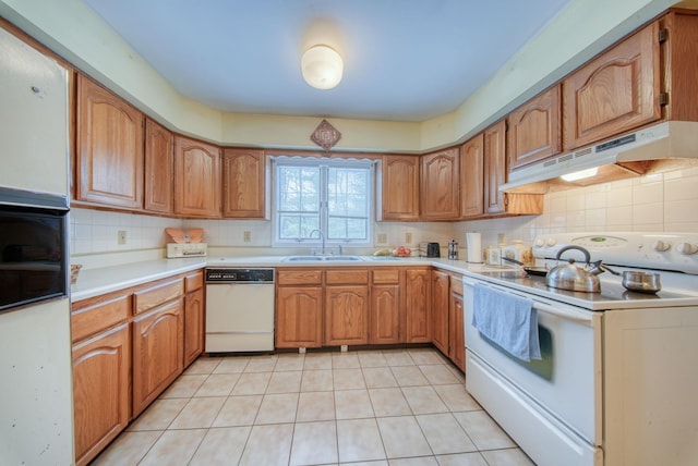 kitchen with white appliances, under cabinet range hood, backsplash, and a sink