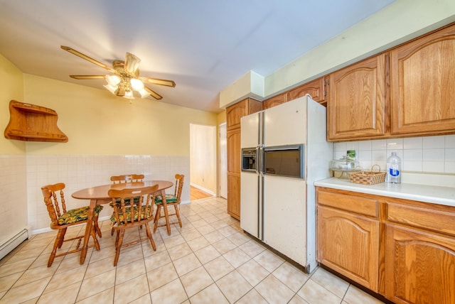 kitchen featuring white refrigerator with ice dispenser, a ceiling fan, a wainscoted wall, baseboard heating, and light countertops