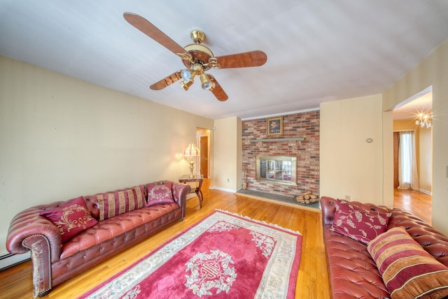 living area with a ceiling fan, a brick fireplace, a baseboard heating unit, and wood finished floors