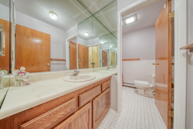 bathroom with toilet, a wainscoted wall, tile patterned floors, vanity, and tile walls