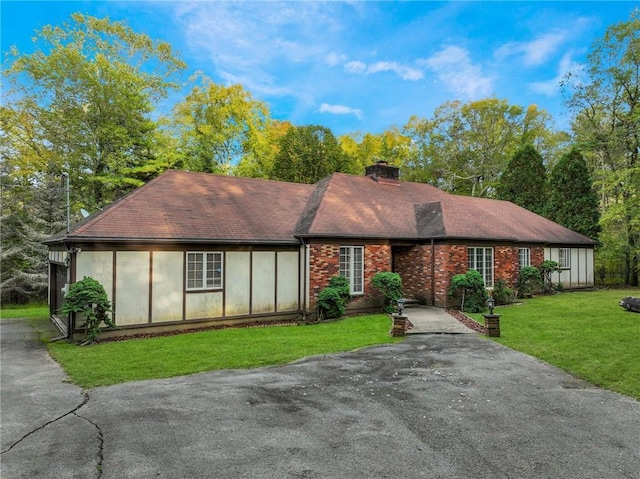 view of front of home with aphalt driveway, brick siding, roof with shingles, a chimney, and a front yard