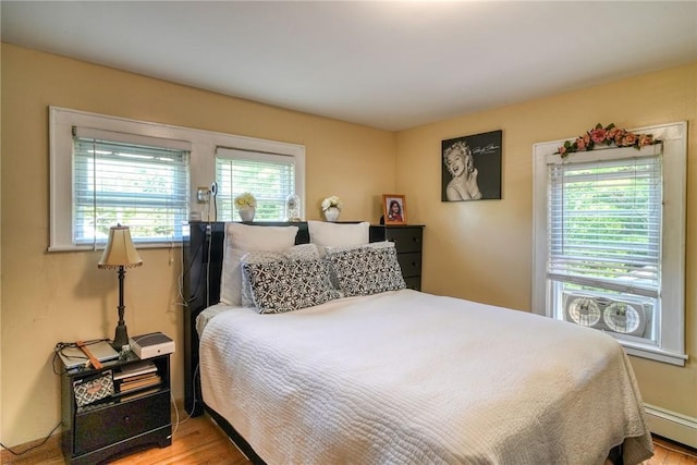 bedroom featuring light hardwood / wood-style floors, baseboard heating, and multiple windows