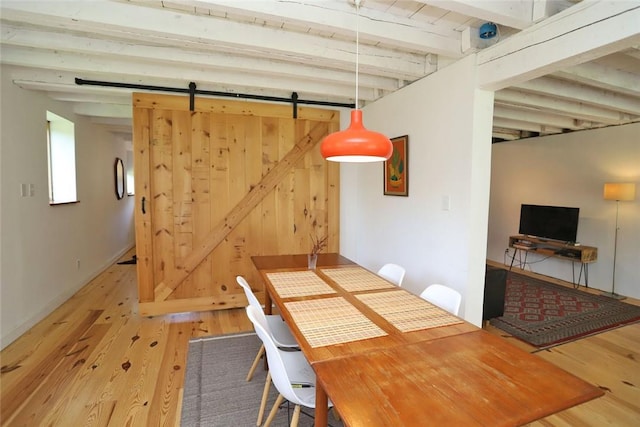 dining area with a barn door, beamed ceiling, and hardwood / wood-style flooring