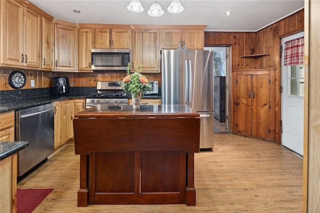 kitchen with a center island, dark stone countertops, light hardwood / wood-style floors, wooden walls, and appliances with stainless steel finishes