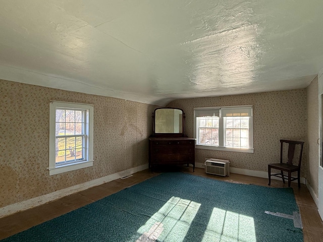 unfurnished room featuring lofted ceiling, hardwood / wood-style flooring, a wall unit AC, and a healthy amount of sunlight