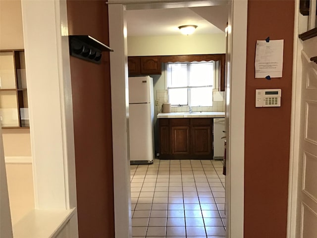 kitchen featuring dark brown cabinets, light tile patterned flooring, white appliances, and sink