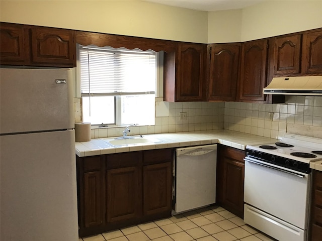 kitchen featuring sink, range hood, tile countertops, white appliances, and light tile patterned floors