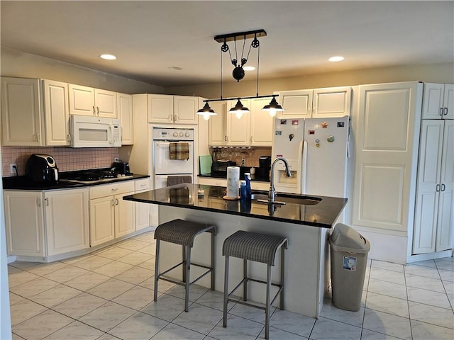 kitchen with pendant lighting, white appliances, decorative backsplash, an island with sink, and white cabinetry