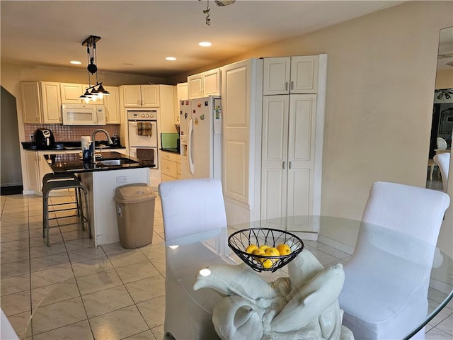 kitchen with decorative backsplash, white appliances, sink, white cabinets, and hanging light fixtures