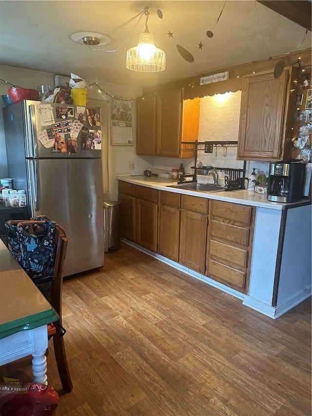 kitchen with sink, decorative light fixtures, stainless steel refrigerator, and light hardwood / wood-style flooring