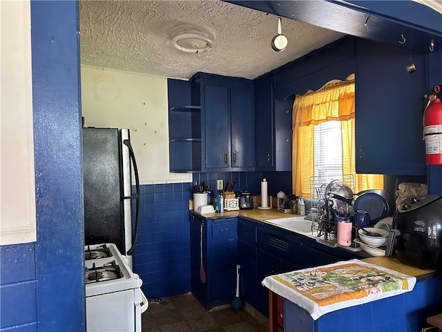 kitchen featuring blue cabinets, a textured ceiling, black refrigerator, tile walls, and white gas range oven