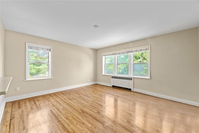 empty room with radiator heating unit, light hardwood / wood-style flooring, and a wealth of natural light