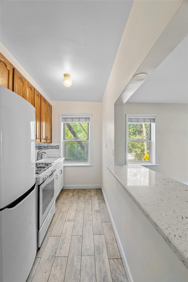 kitchen with light wood-type flooring, white refrigerator, a healthy amount of sunlight, and stainless steel gas range