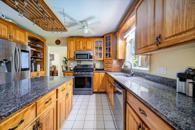 kitchen with ceiling fan, sink, stainless steel appliances, dark stone counters, and light tile patterned floors