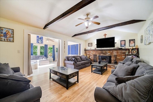 living room with vaulted ceiling with beams, ceiling fan, light wood-type flooring, and a wood stove