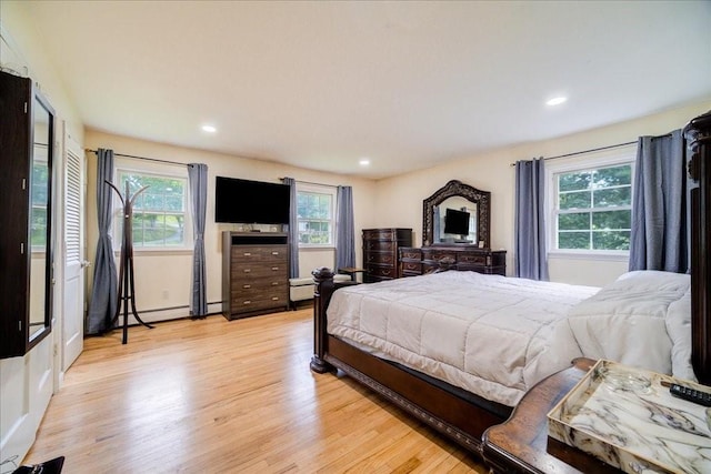 bedroom with light hardwood / wood-style floors, a baseboard heating unit, and multiple windows