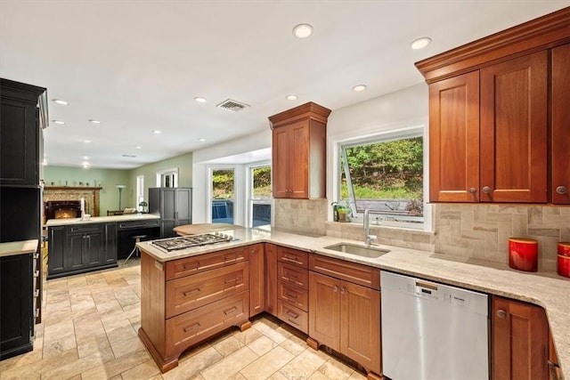 kitchen with kitchen peninsula, appliances with stainless steel finishes, tasteful backsplash, light stone counters, and sink