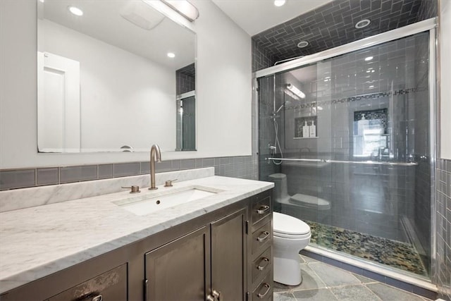 bathroom with vanity, toilet, a shower with door, and tile walls