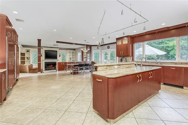 kitchen with decorative backsplash, light tile patterned flooring, light stone countertops, and a large island with sink